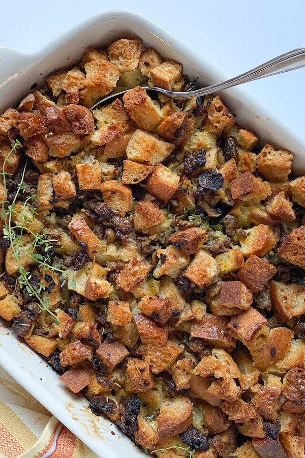 Golden brown Thanksgiving stuffing in a ceramic baking dish, topped with crispy bread cubes and herbs
