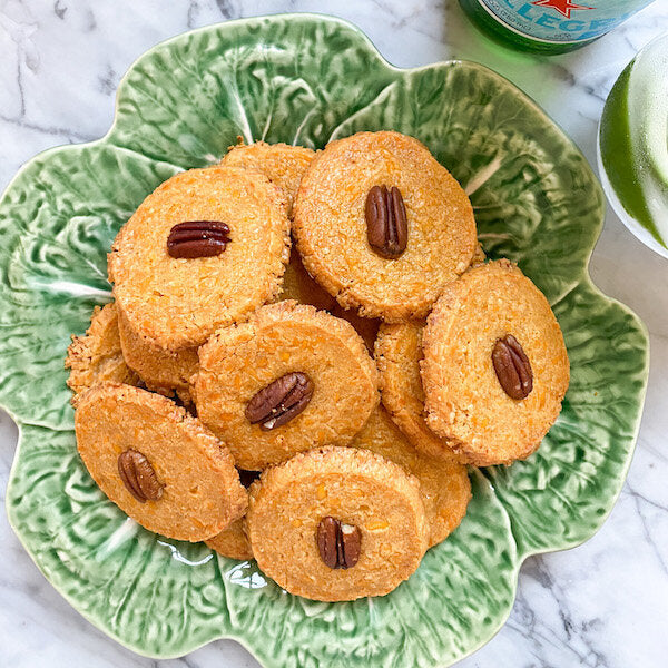 Golden brown pecan cheese wafers arranged on a serving platter, each topped with a whole pecan