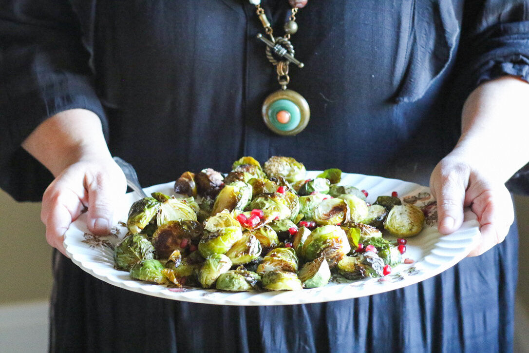 Golden brown roasted Brussels sprouts with caramelized edges, topped with bright red pomegranate seeds on a serving platter