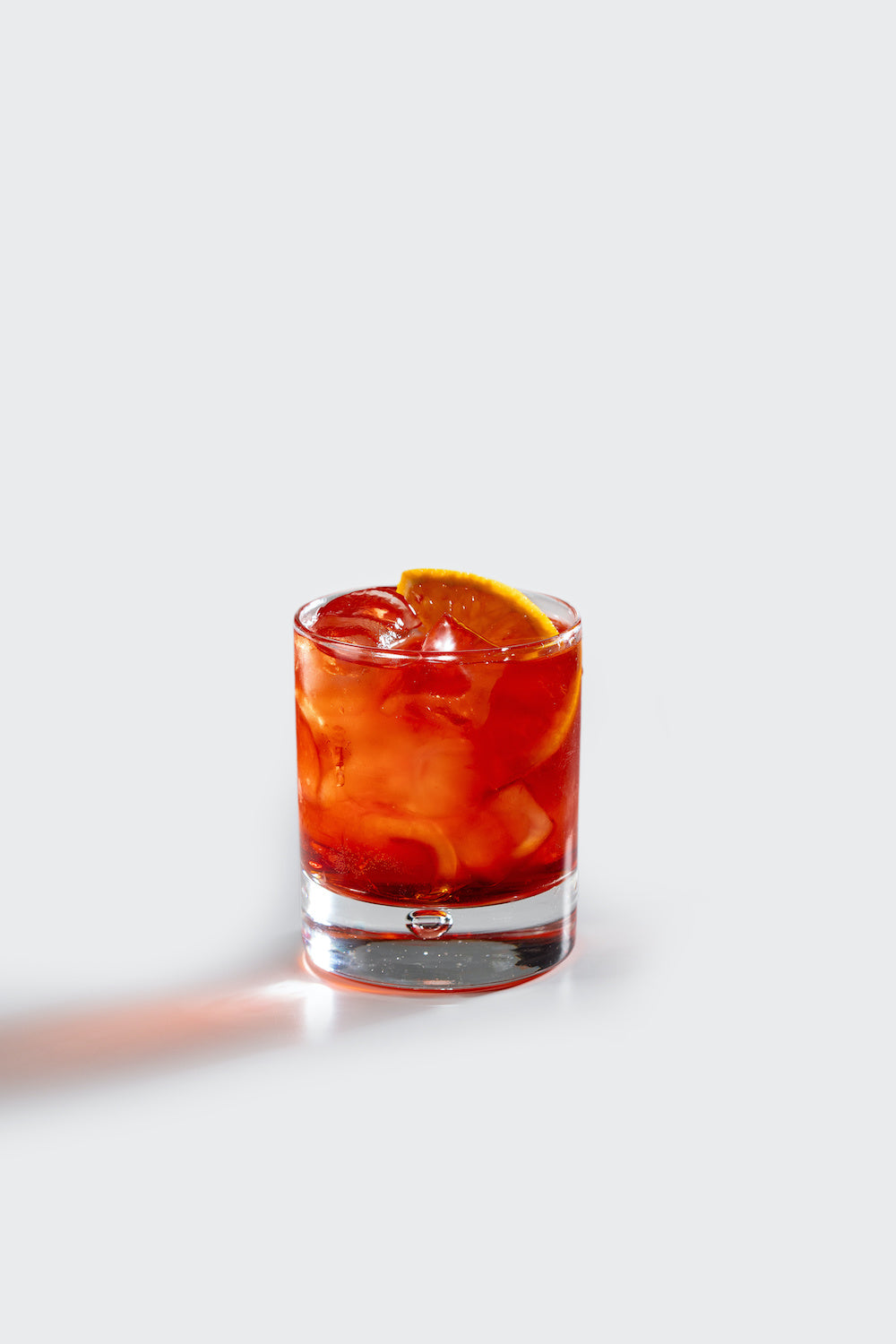 A Boulevardier cocktail served in a clear rocks glass over a large ice cube, garnished with a Boozy Cocktail Cherry® and orange peel