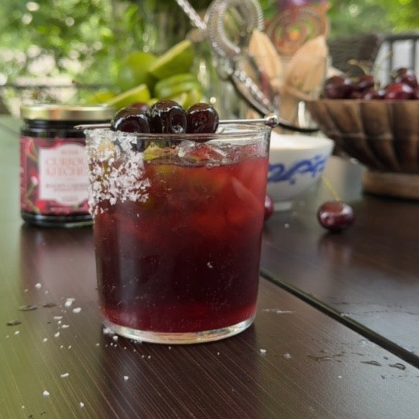 Cherry Batanga tequila cocktail with Coca-Cola, fresh cherries, amaretto, and lime, served over ice in a kosher salt-rimmed glass with Boozy Cocktail Cherries.