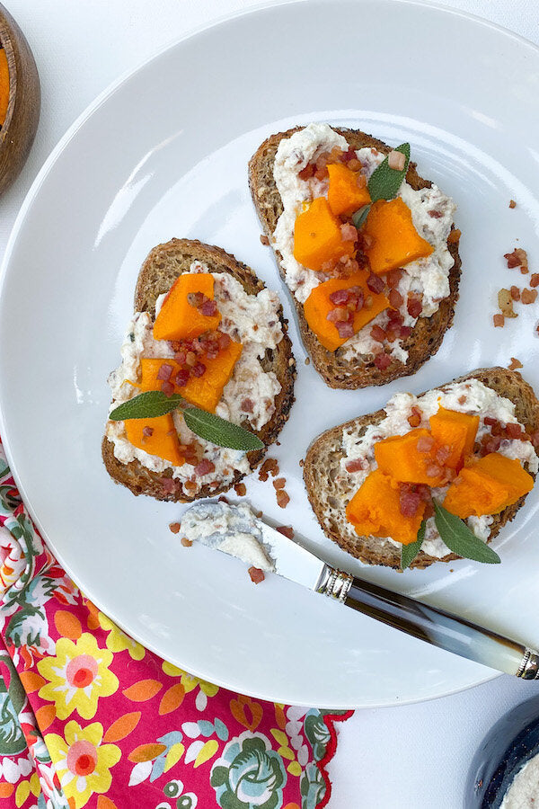 Golden pumpkin crostini topped with creamy ricotta, roasted pumpkin cubes, and crispy pancetta on rustic seedy bread