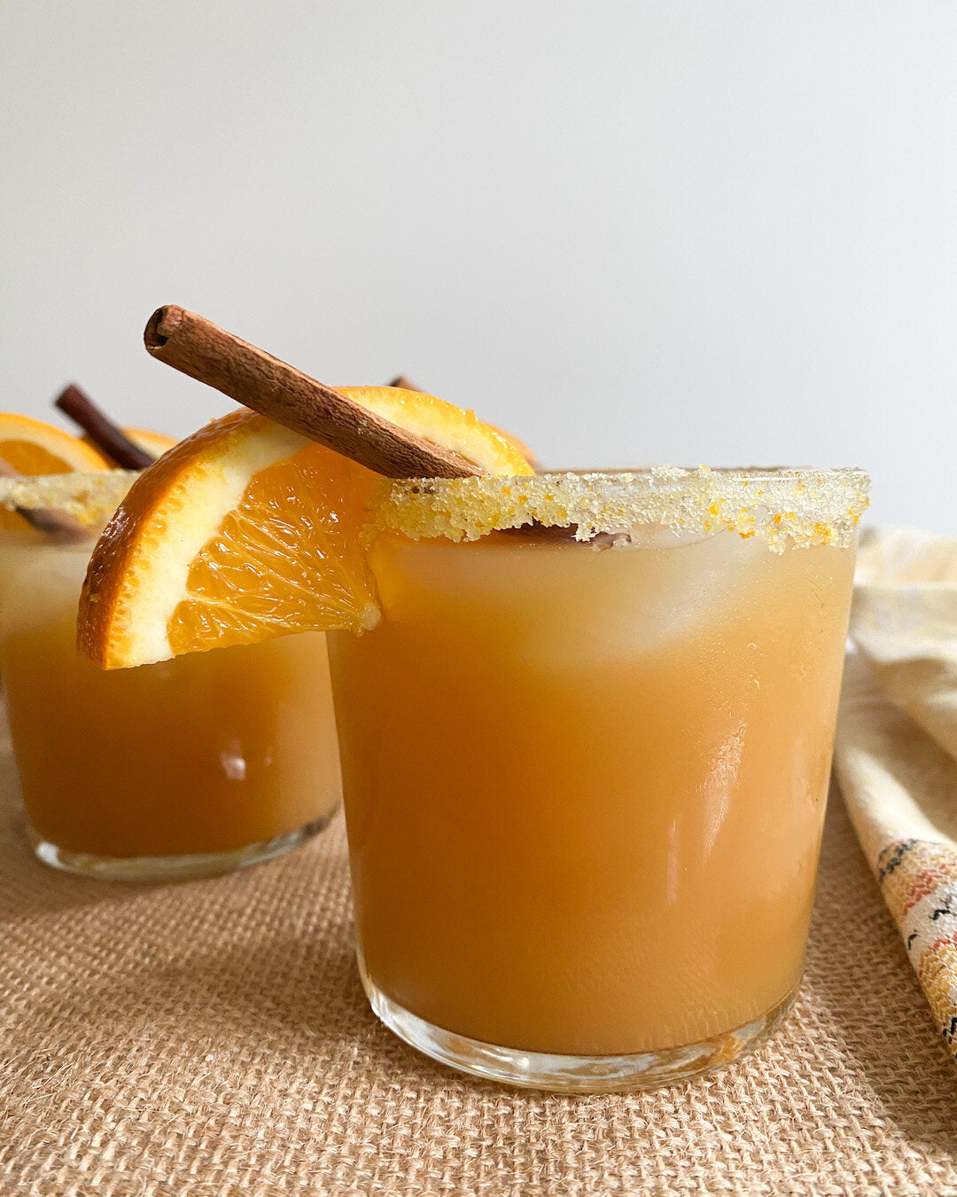 Bourbon apple cider in glasses with orange sugar rim, garnished with orange slices and cinnamon sticks