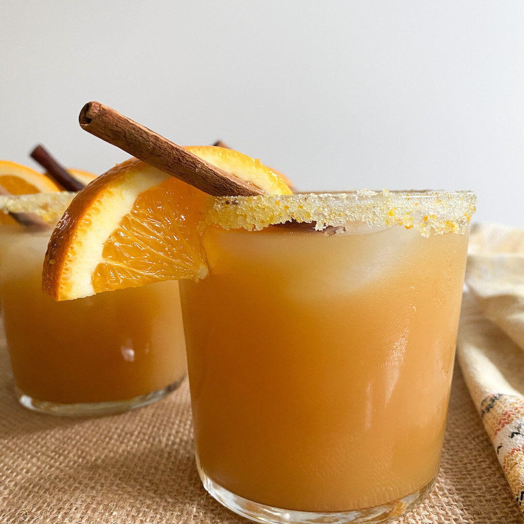 Bourbon apple cider in glasses with orange sugar rim, garnished with orange slices and cinnamon sticks
