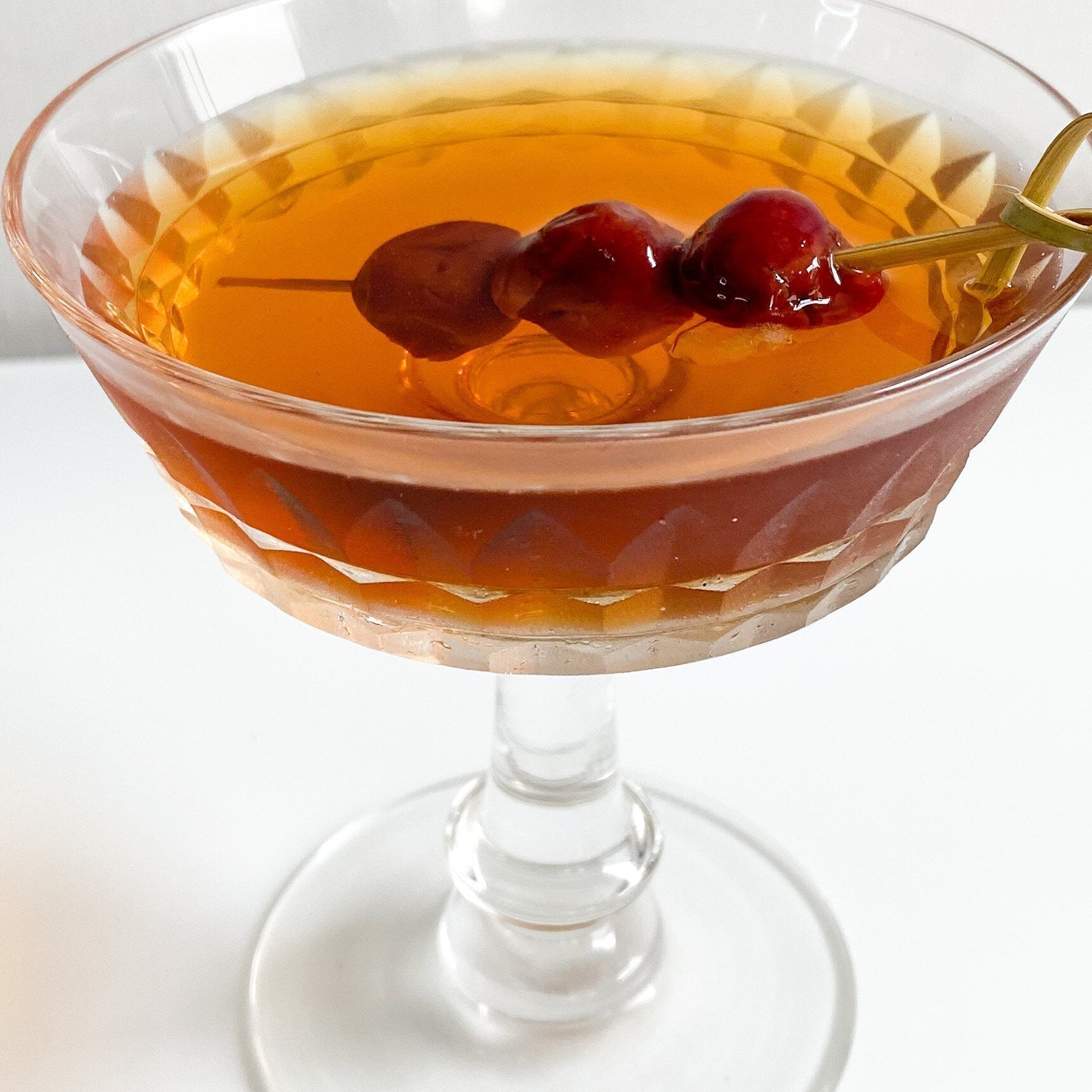 Classic Manhattan cocktail with rye whiskey, sweet vermouth, bitters, and cocktail cherries served in a chilled coupe glass.