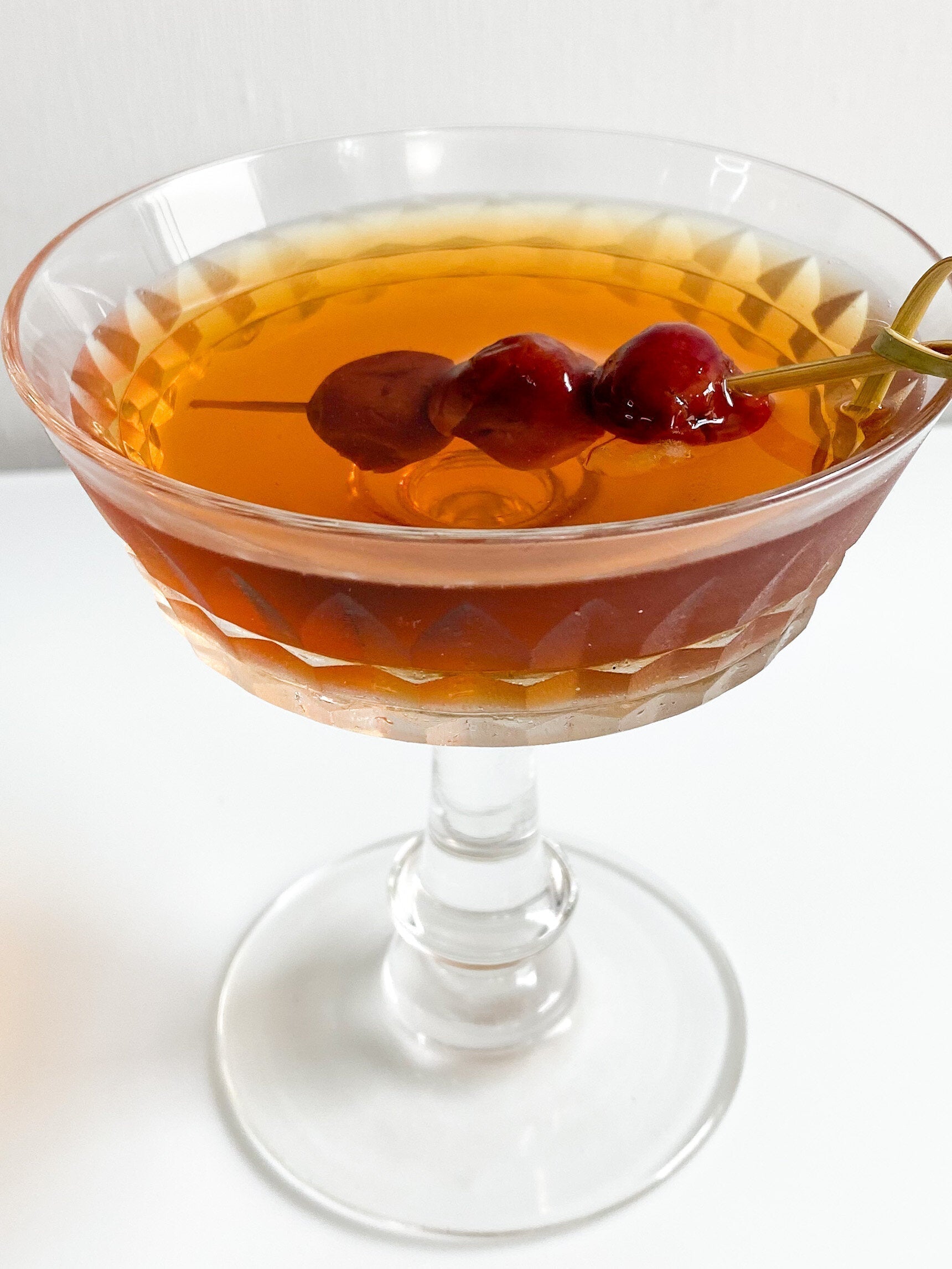 Classic Manhattan cocktail with rye whiskey, sweet vermouth, bitters, and cocktail cherries served in a chilled coupe glass.