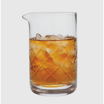Clear glass with a textured bottom filled with iced amber liquid on a light gray background